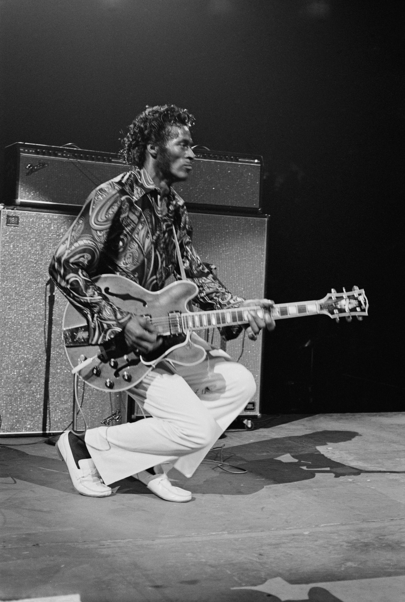 Black and white photograph of Chuck Berry crouching mid-performance with his guitar at Madison Square Garden, New York, 1971