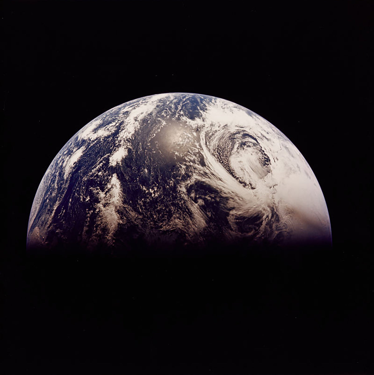 Colour photograph of a crescent of Earth against black space from Apollo 13, with a large storm swirling over the North Pacific, 1970