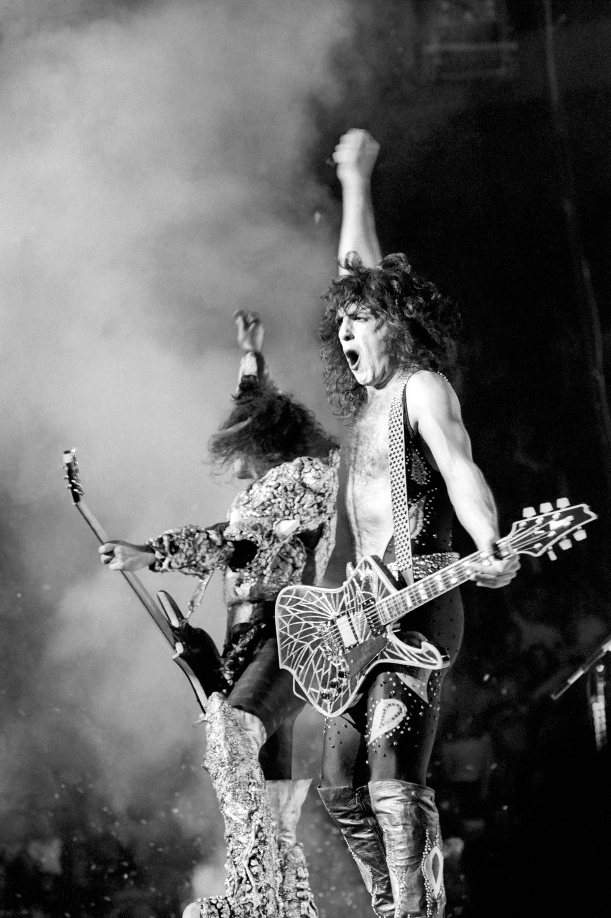 Black and white photograph of Paul Stanley and Gene Simmons of Kiss performing in costume amid stage smoke, Los Angeles, 1979