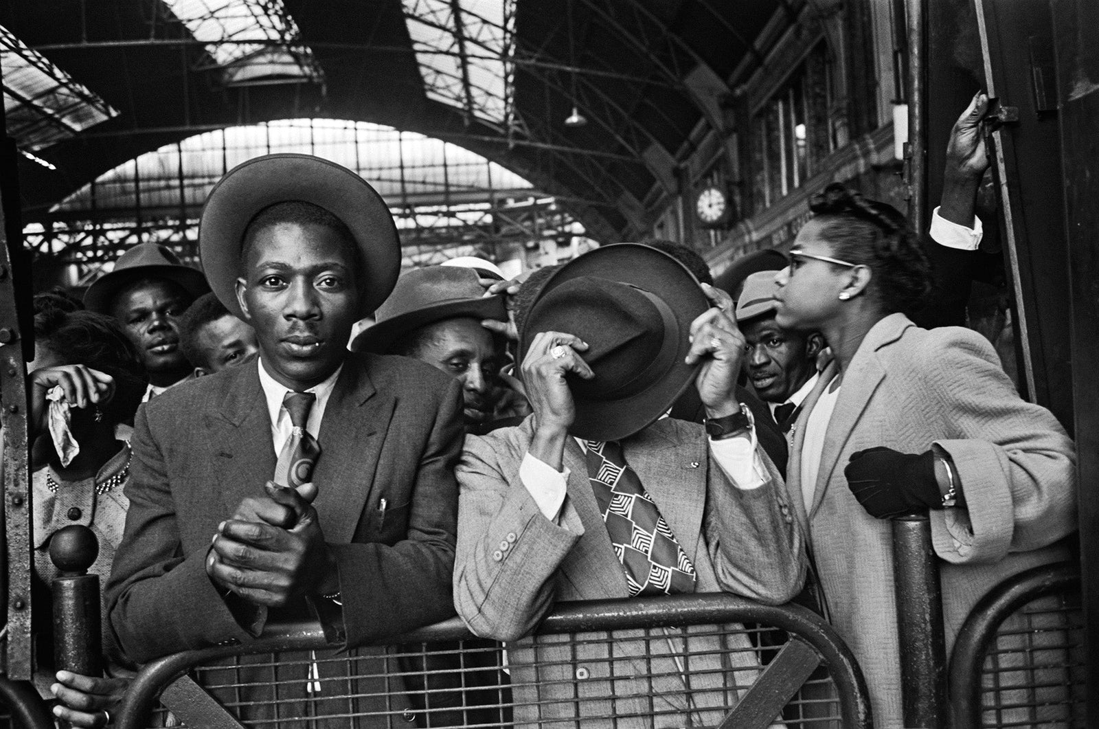 Black and white photograph of West Indian arrivals in hats and overcoats on the platform at Victoria Station, London, 1956