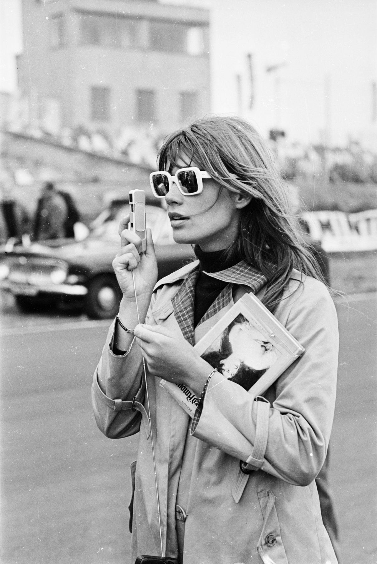 Black and white photograph of Francoise Hardy in white sunglasses and a trench coat at Brands Hatch race circuit
