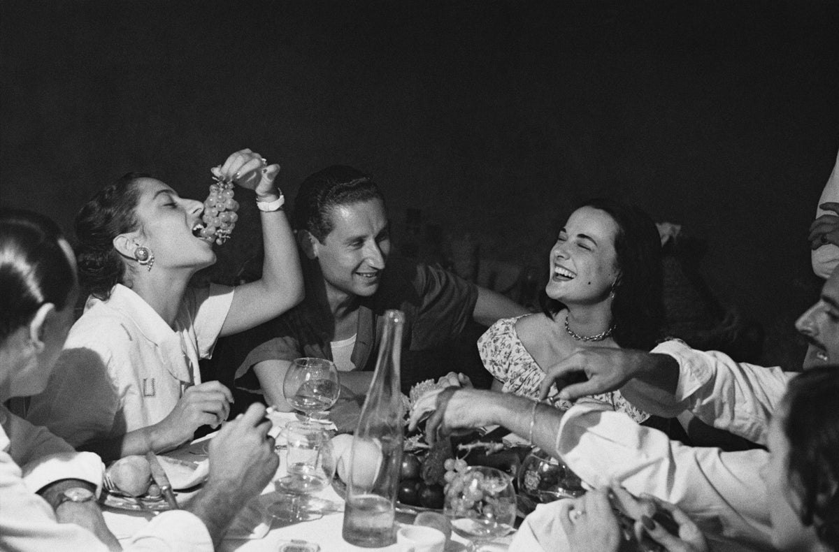 Black and white photograph of young women laughing and feeding each other grapes at a lively party in Positano, Italy, 1949