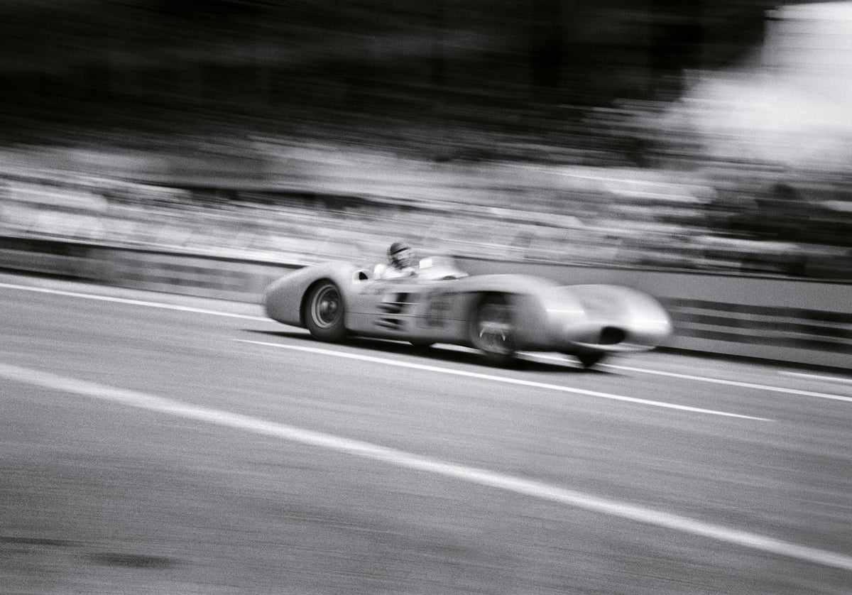Black and white photograph of Juan Manuel Fangio's Mercedes streaking past in a motion blur at the French Grand Prix in Reims, 1954