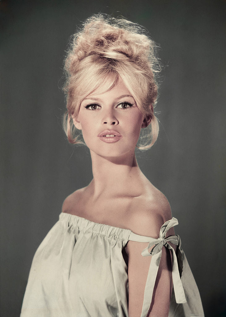 Colour studio portrait of Brigitte Bardot with a blonde beehive wearing a pale off-the-shoulder dress, circa 1960