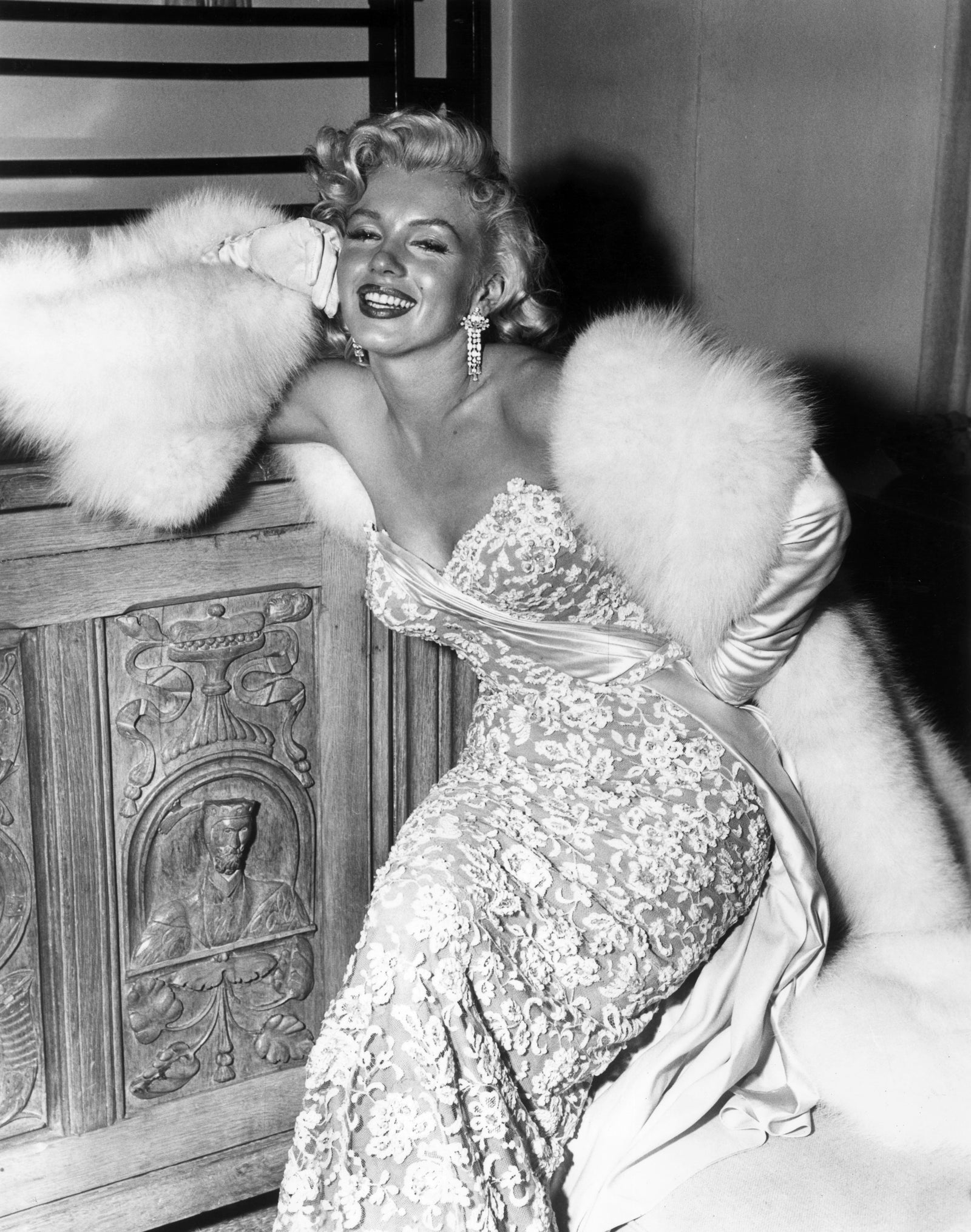 Black and white photograph of a smiling Marilyn Monroe in a lace evening gown and white fur stole, 1953