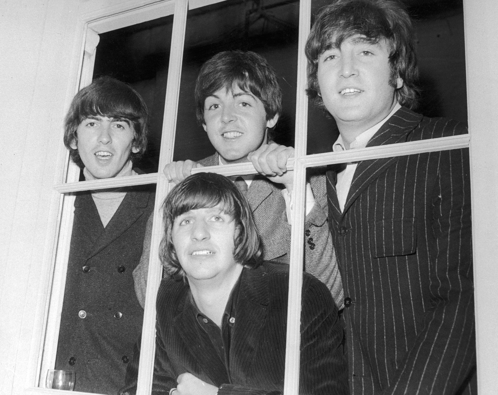 Black and white photograph of The Beatles peering out through a window at Twickenham Film Studios, 1965
