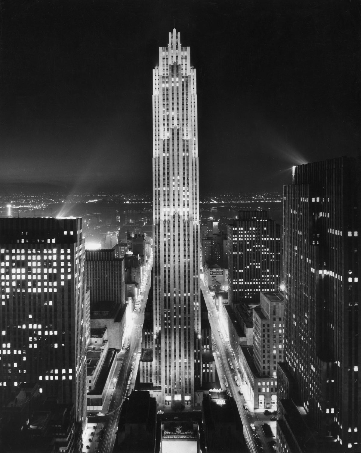 Black and white photograph of the Rockefeller Center tower lit up at night above the Manhattan skyline, circa 1945
