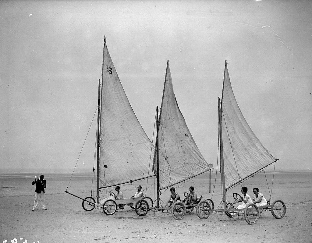 Black and white photograph of three sand yachts with tall sails lined up on a wide French beach, 1927
