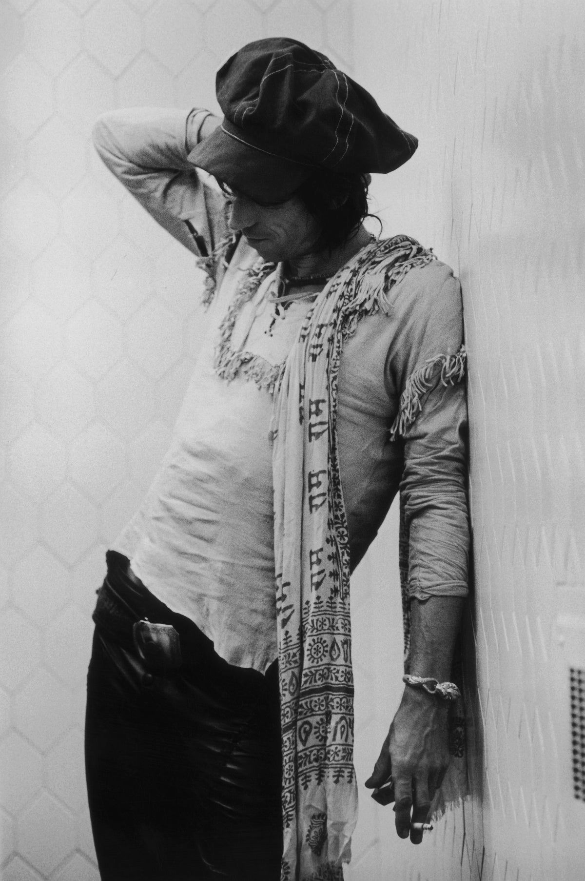 Black and white photograph of Keith Richards in a cap and scarf leaning against a wall on the Rolling Stones' 1975 tour