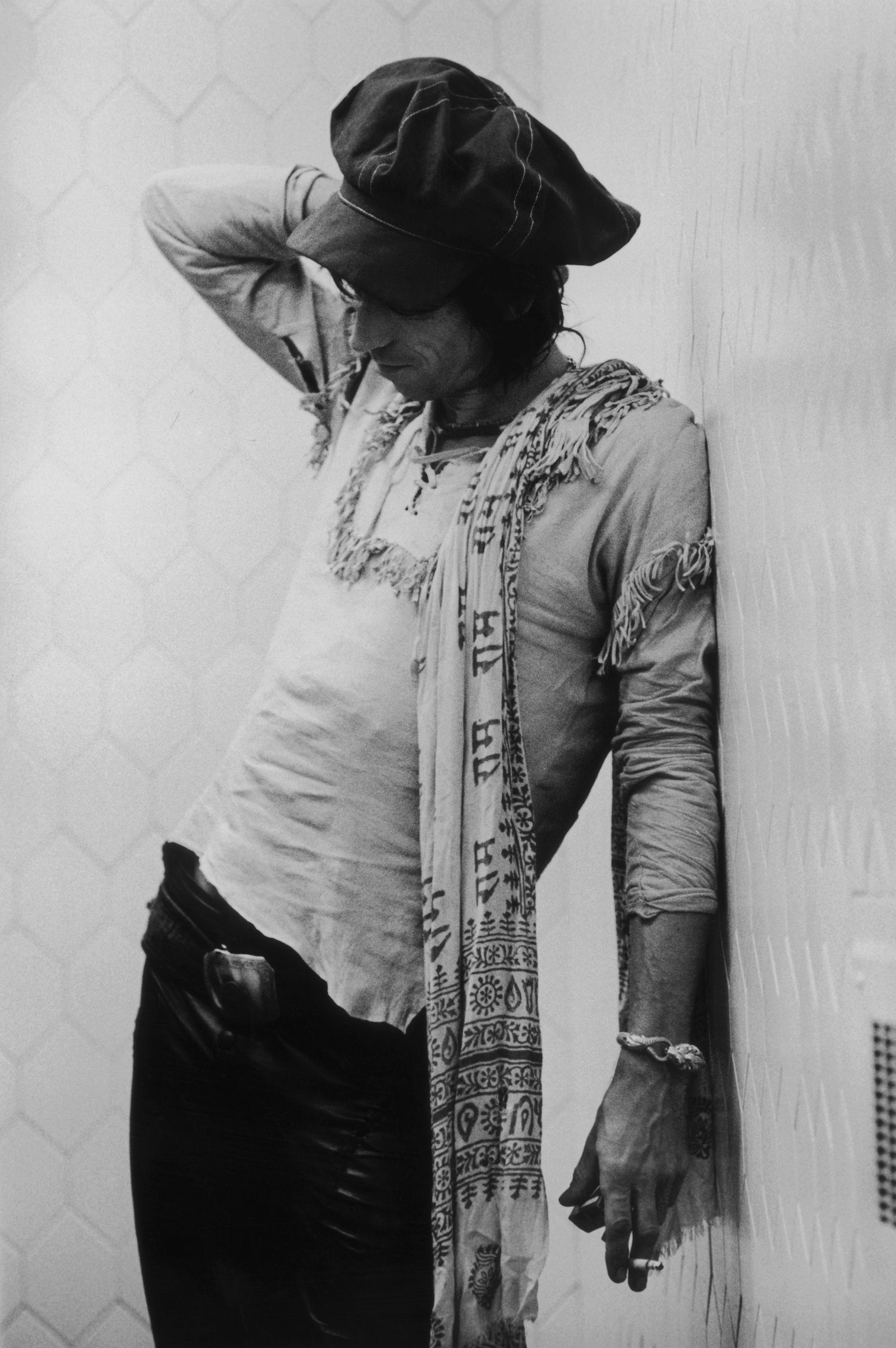 Black and white photograph of Keith Richards in a cap and scarf leaning against a wall on the Rolling Stones' 1975 tour
