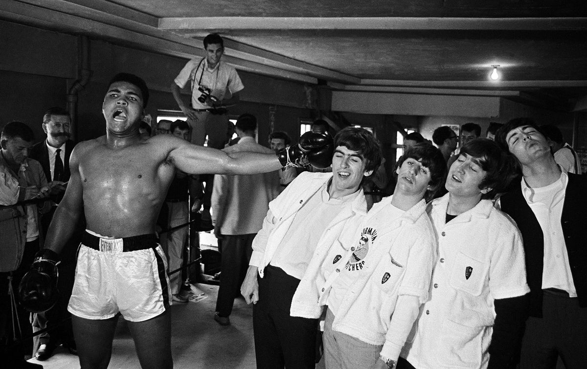 Black and white photograph of Cassius Clay in the boxing ring playfully squaring up to the four Beatles in Miami, 1964