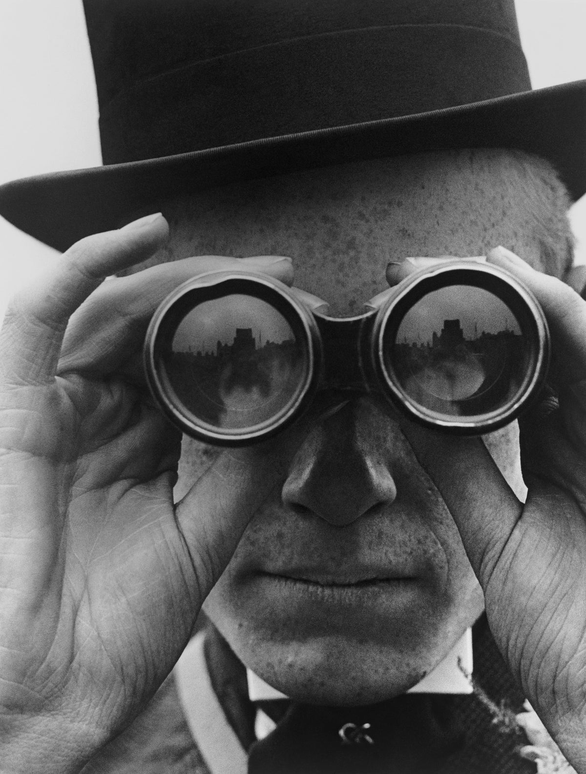 Black and white close-up of a man in a top hat looking through binoculars at the Derby, Epsom, 1923