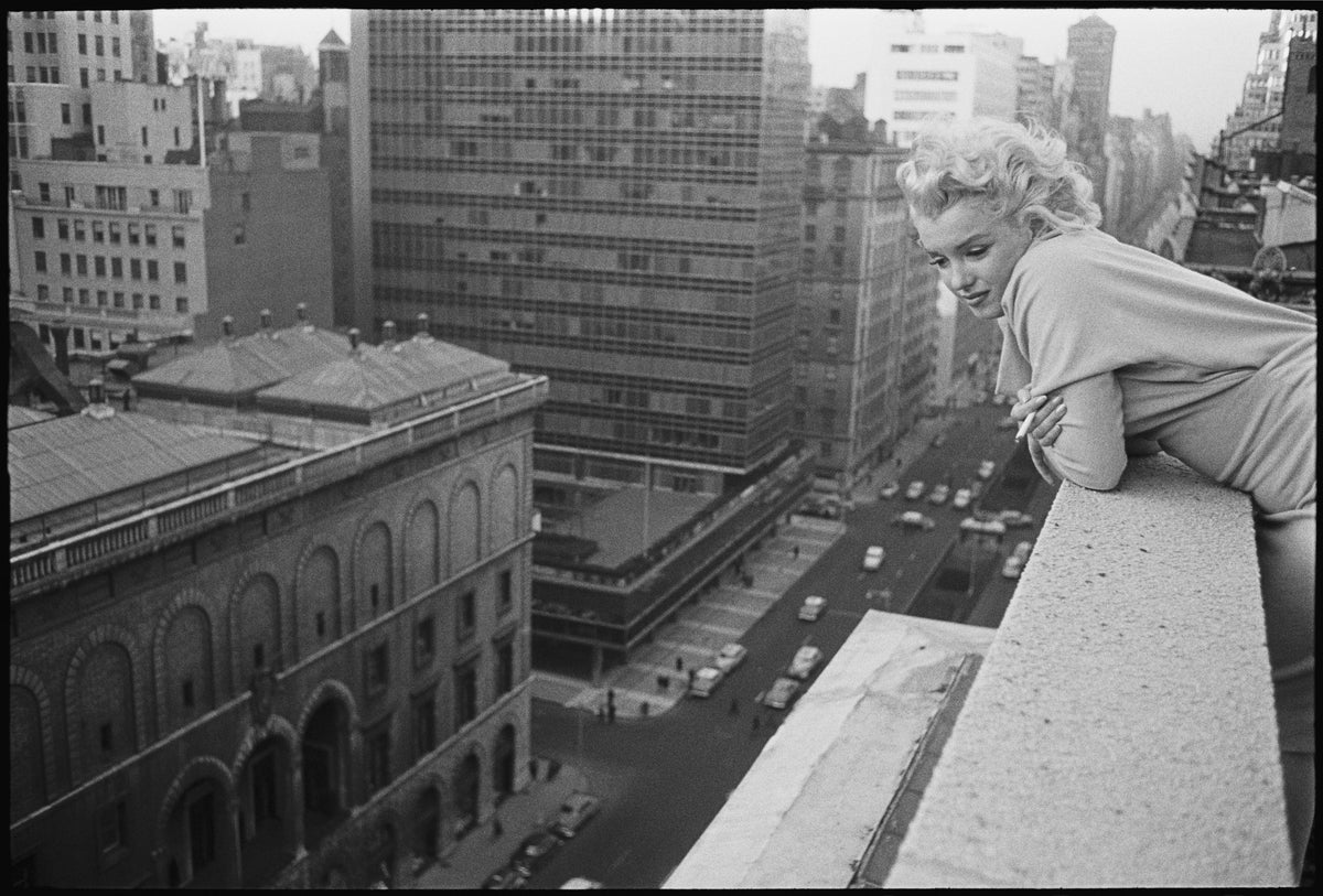 Black and white photograph of Marilyn Monroe leaning over the edge of the Ambassador Hotel roof high above Manhattan, 1955