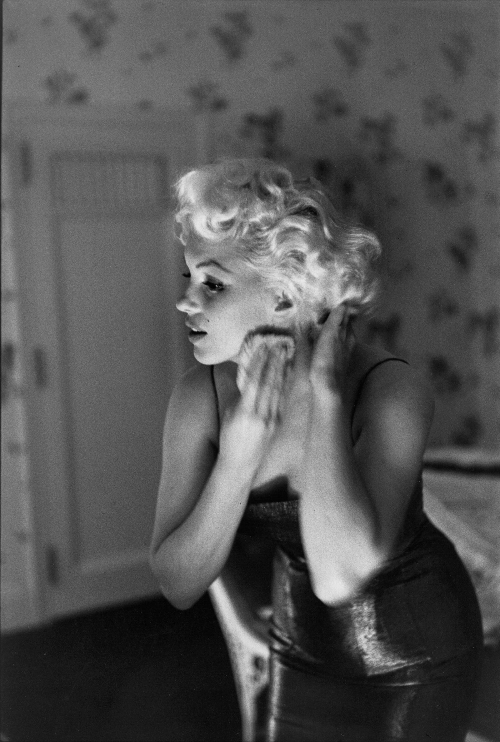 Black and white photograph of Marilyn Monroe dabbing on perfume as she gets ready in her room at the Ambassador Hotel, New York, 1955