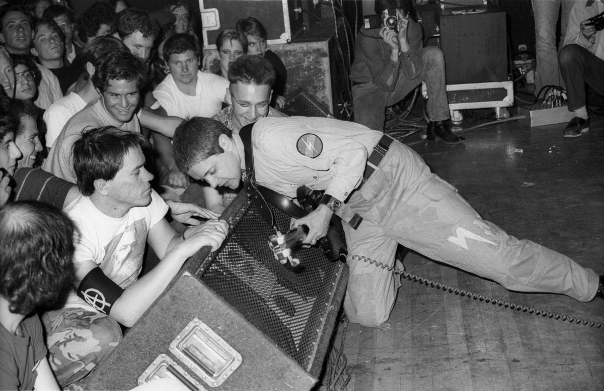 Black and white photograph of Genesis P-Orridge of Throbbing Gristle sprawled on stage in front of a packed crowd, Culver City, 1981
