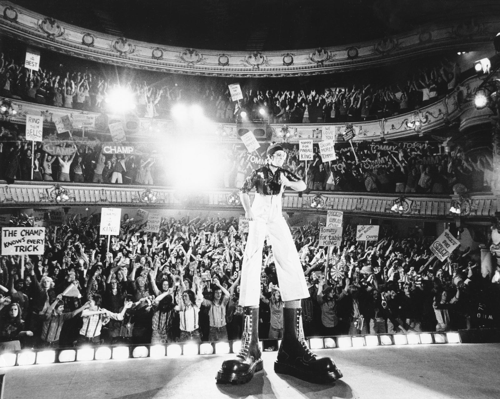 Black and white photograph of Elton John in giant Doc Martens boots on stage as the Pinball Wizard in the film Tommy, 1975