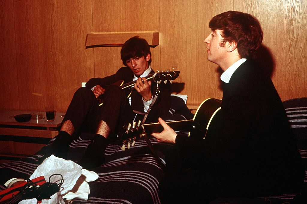Colour photograph of George Harrison and John Lennon playing guitars as they rehearse in their Stockholm hotel room, 1963