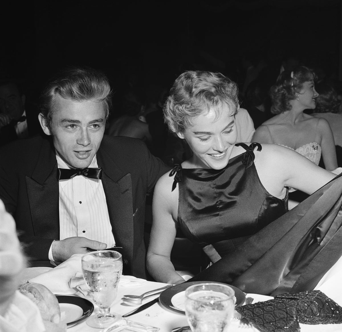 Black and white photograph of James Dean in a dinner jacket and Ursula Andress at a table at Ciro's nightclub, Los Angeles, 1955