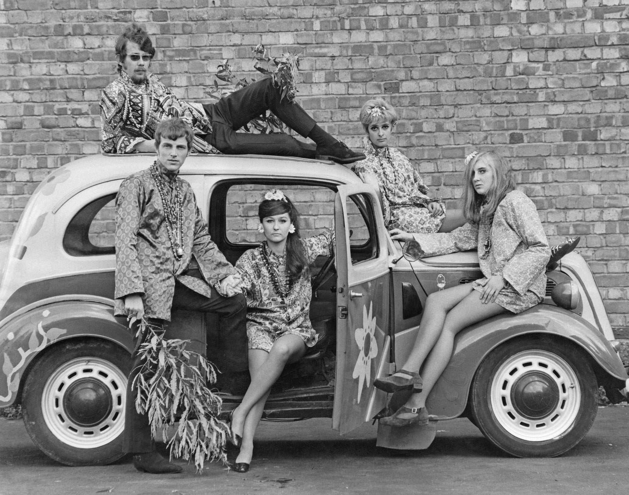Hippiemobile by Express/Getty Images, 1968. Young men and women pose in and on a car while modeling factory-made versions of Flower Power clothing, England.. Open Edition Resin Photographic Print. Portrait orientation. Available at Electric Gallery, London, UK.