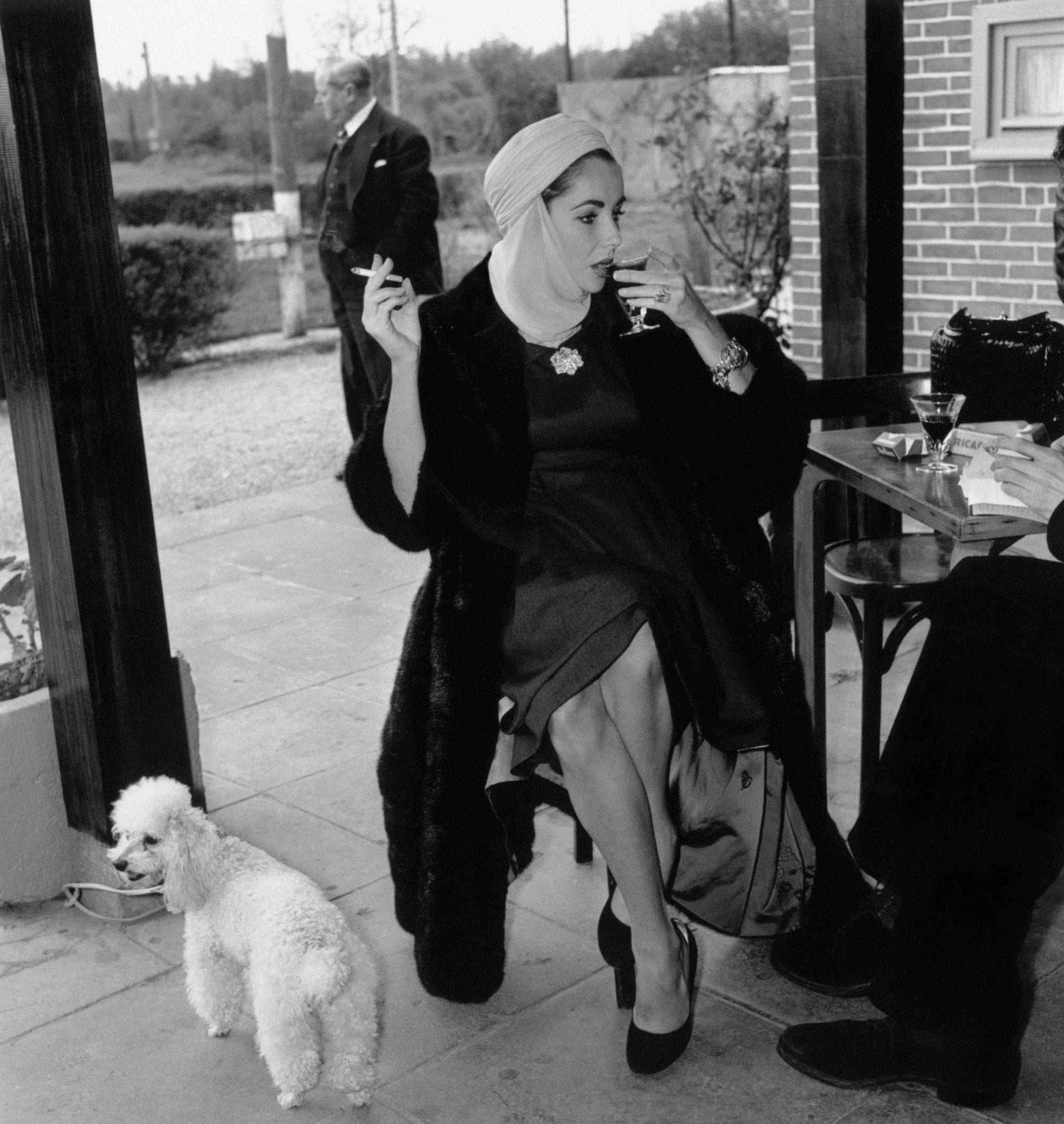 Taylor And Poodle by Express/Getty Images, 1957. American actress Elizabeth Taylor sips a drink and smokes a cigarette during a stop for interviews at Jersey airport en route to Nice.. Open Edition Resin Photographic Print. Square orientation. Available at Electric Gallery, London, UK.