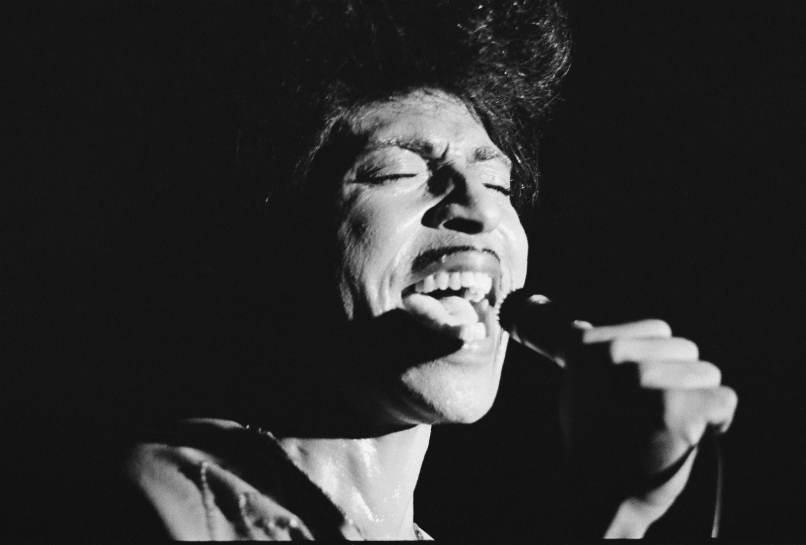 Black and white close-up of Little Richard singing passionately into a microphone on a dark stage, UK, 1975