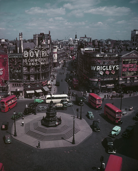 Colour photograph looking down on Piccadilly Circus with red buses, neon advertisements and the Eros statue, London, circa 1954