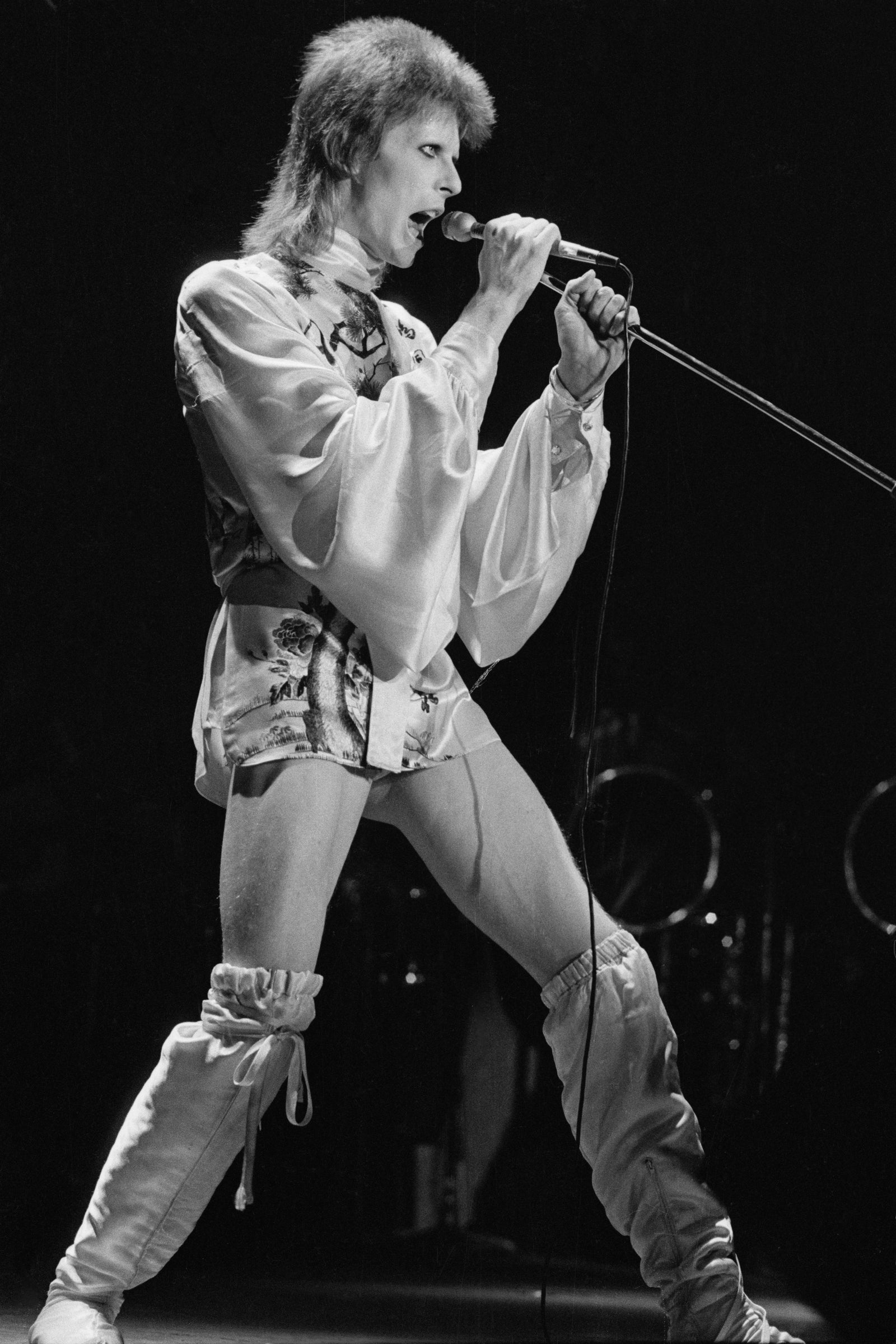 Black and white photograph of David Bowie as Ziggy Stardust singing at the microphone at his final Hammersmith Odeon show, London, 1973