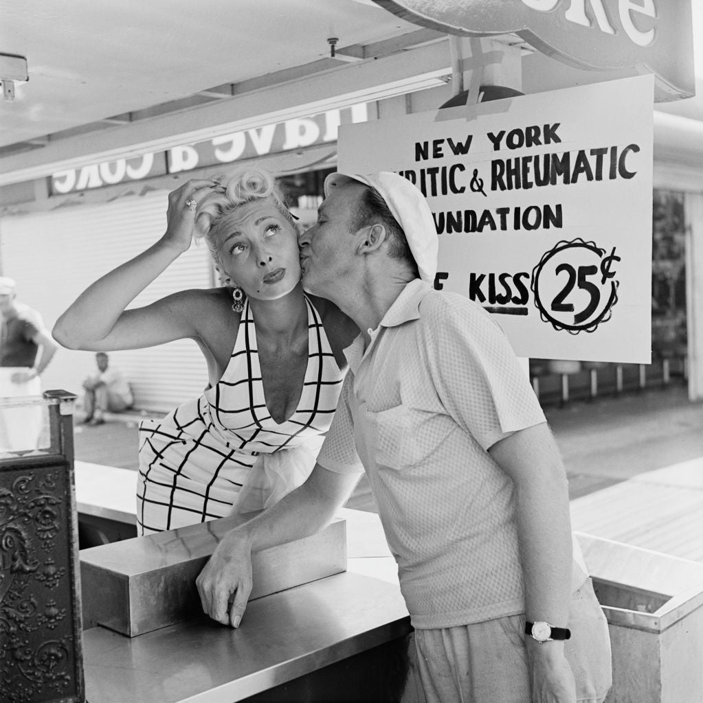 Black and white photograph of a sailor kissing a woman on the cheek at a 25 cent charity kissing booth in New York, 1953