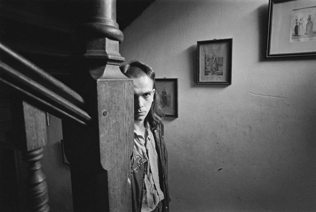 Black and white photograph of Peter Gabriel peering out from behind a wooden staircase, UK, 1974