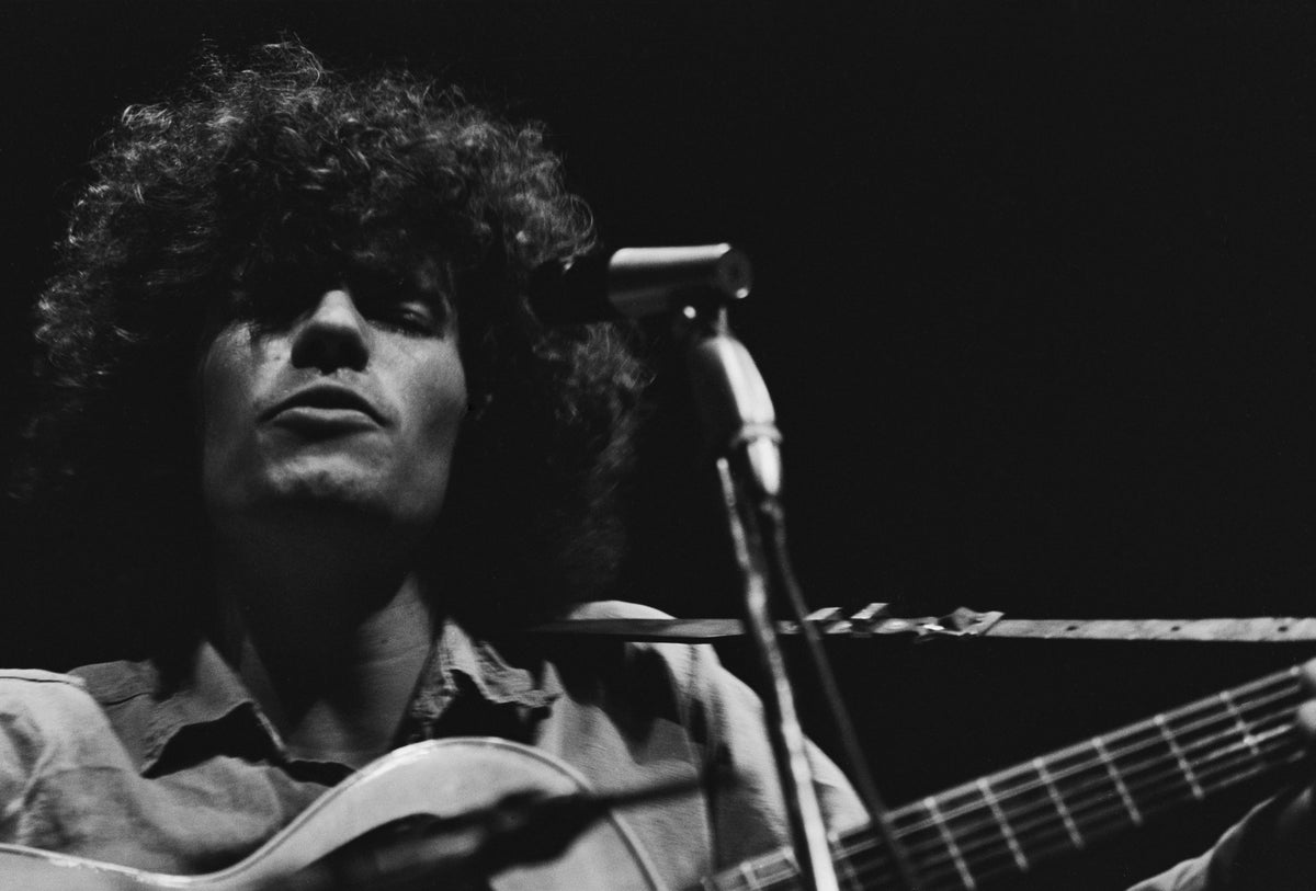 Black and white close-up of Tim Buckley singing at a microphone with his acoustic guitar, circa 1967