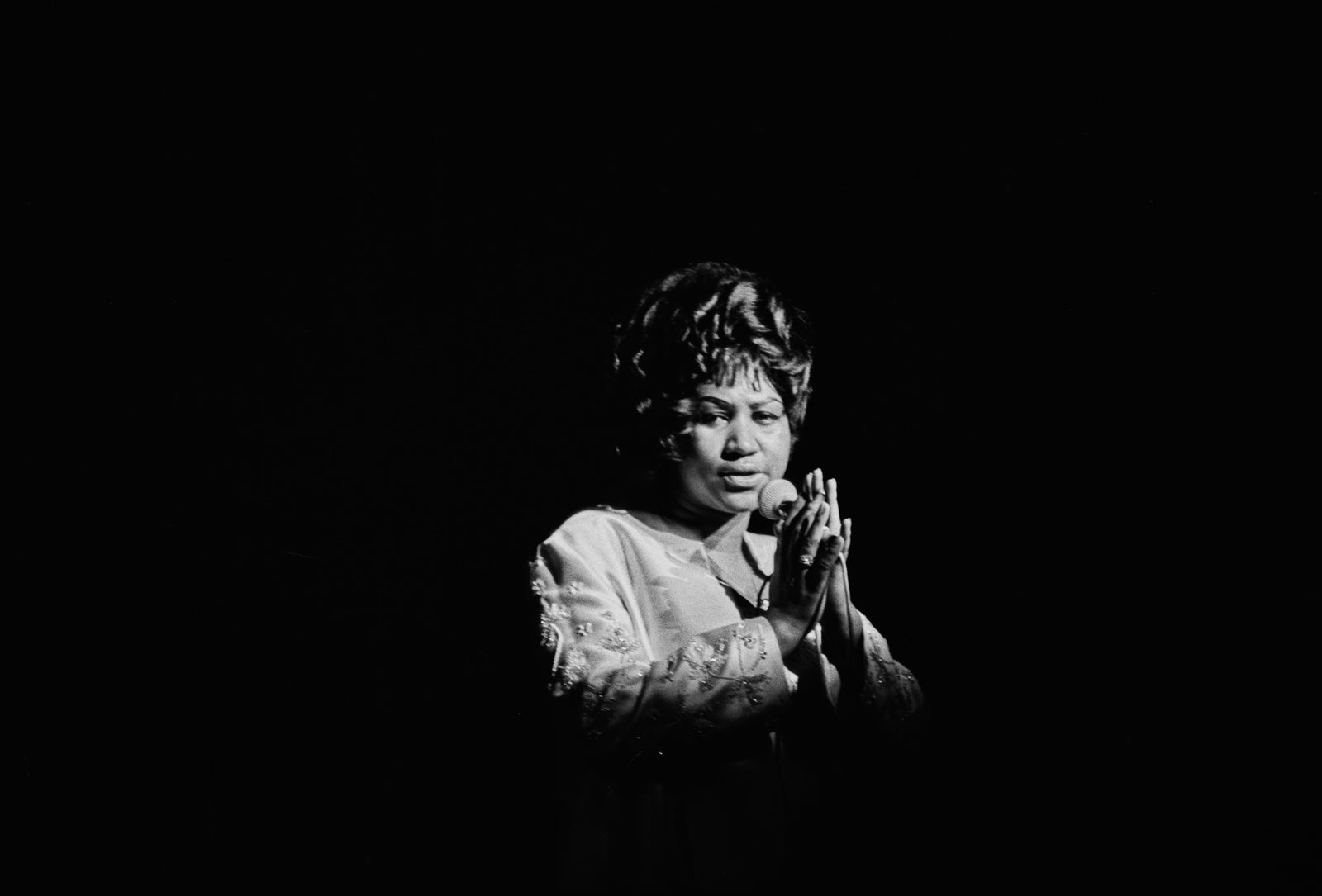 Black and white photograph of Aretha Franklin singing in a single spotlight on a dark stage at Philharmonic Hall, New York, 1968