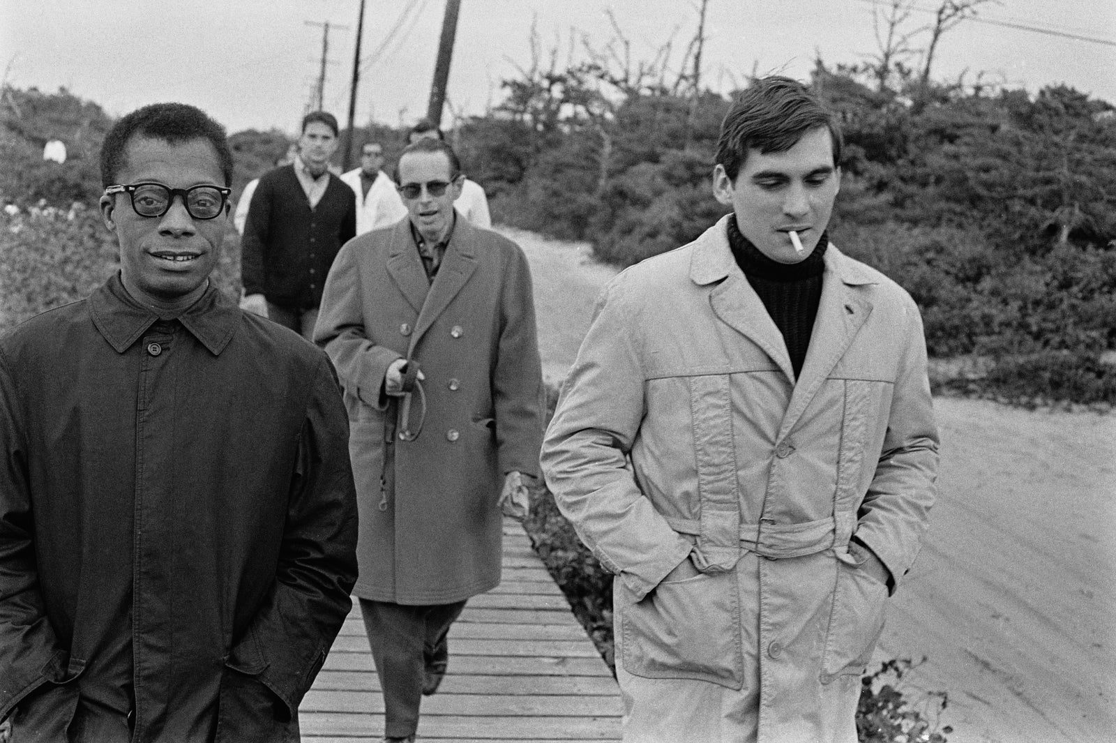 Black and white photograph of James Baldwin walking along a boardwalk with friends, USA, 1963