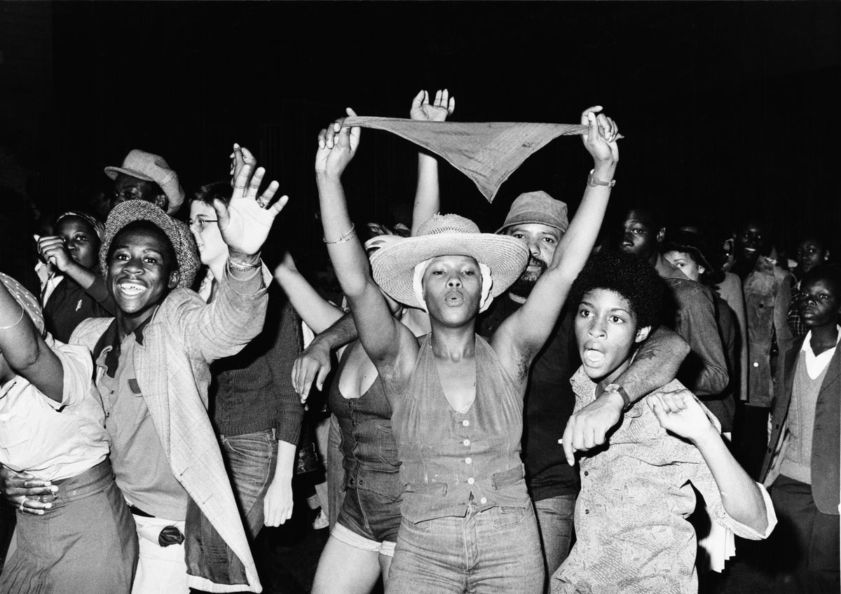 Black and white photograph of young people dancing and cheering with arms raised at the Notting Hill Carnival, London, 1976