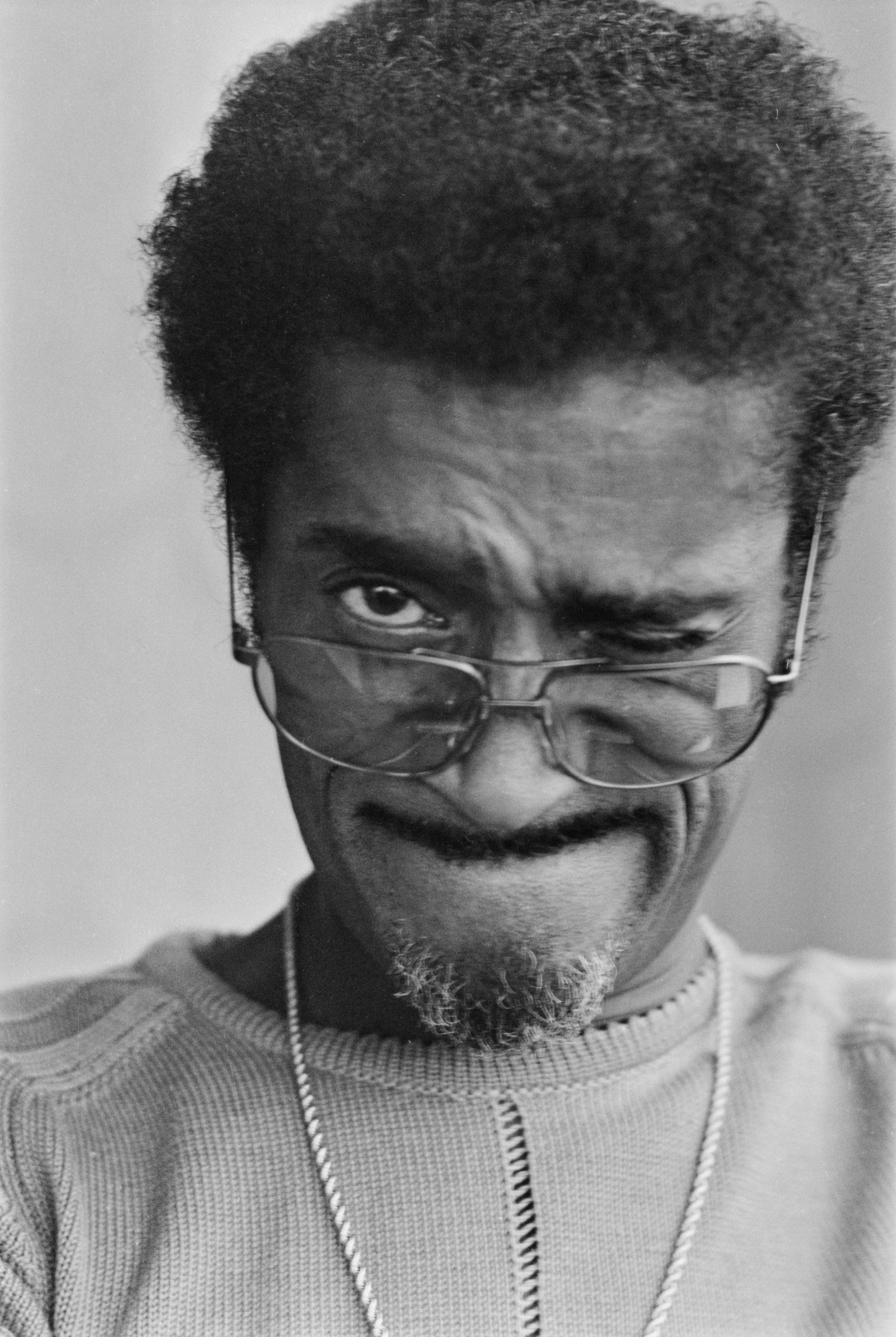 Black and white close-up of Sammy Davis Jr pulling a comic face, squinting one eye behind his glasses, London, 1972