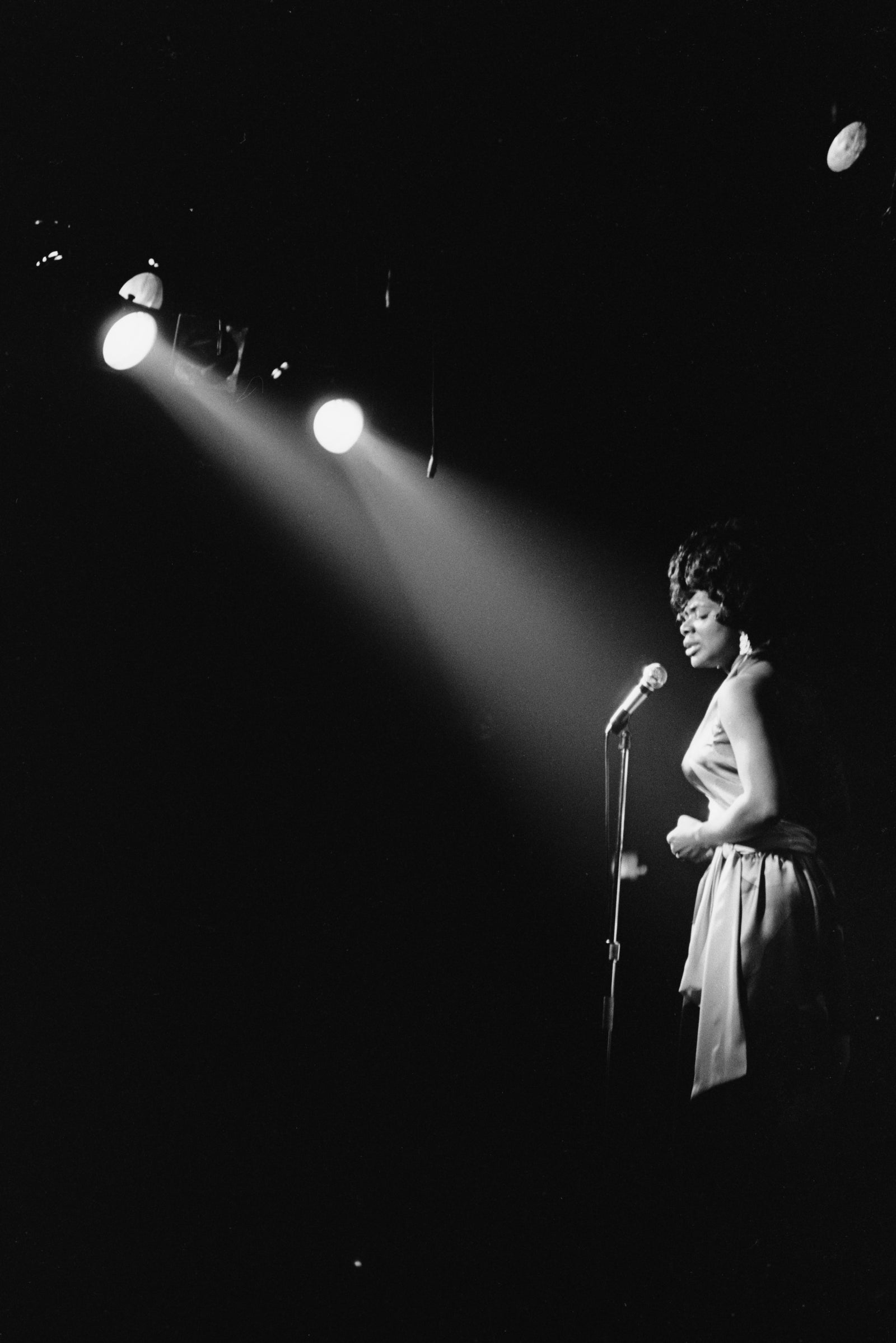Black and white photograph of Carla Thomas singing at a microphone under spotlights at the Village Gate, New York, 1969