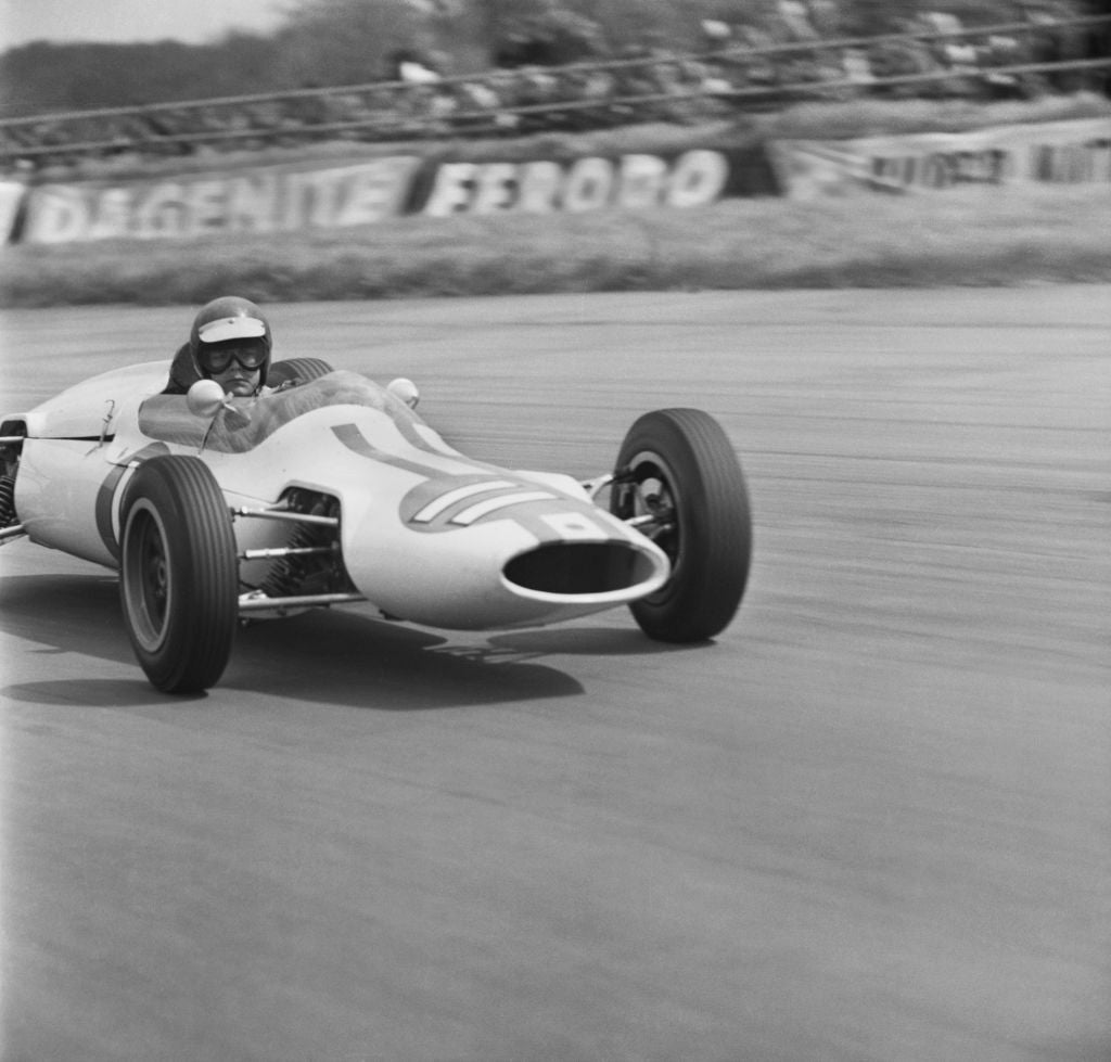 Black and white photograph of racing driver Peter Revson at speed in a Cooper Formula Junior car at Silverstone, 1963