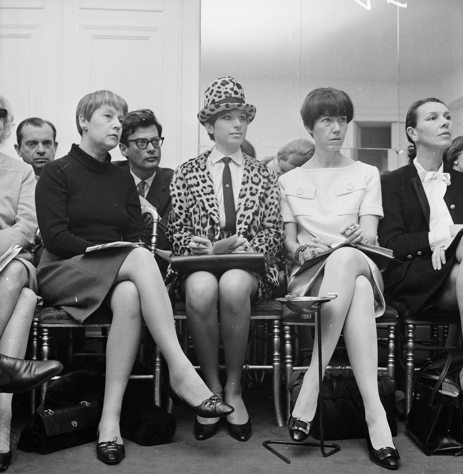 Black and white photograph of Barbra Streisand in a leopard print suit and hat seated in the front row at a Chanel show in Paris