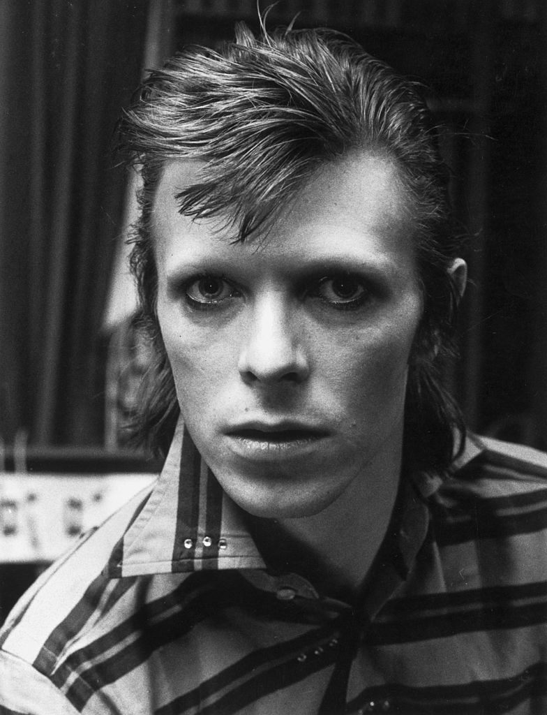 Black and white close-up portrait of David Bowie with spiky hair and a striped shirt, staring into the camera, 1973