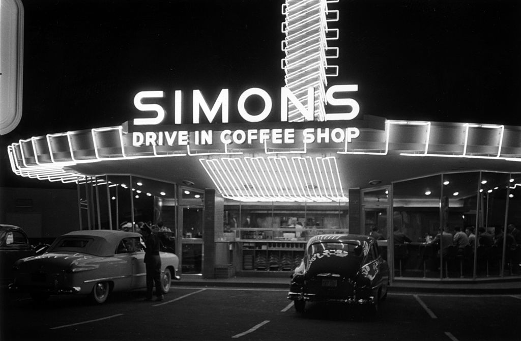 Black and white photograph of the neon-lit Simons Drive-In Coffee Shop at night with cars parked outside, Hollywood, 1951