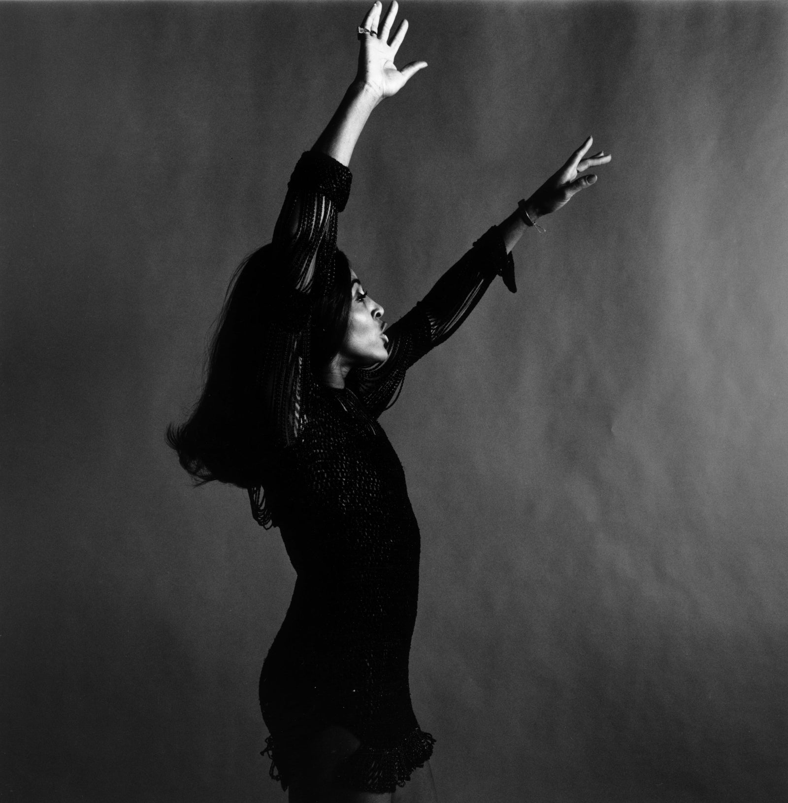 Black and white studio photograph of Tina Turner dancing in profile with both arms raised above her head, New York, 1969