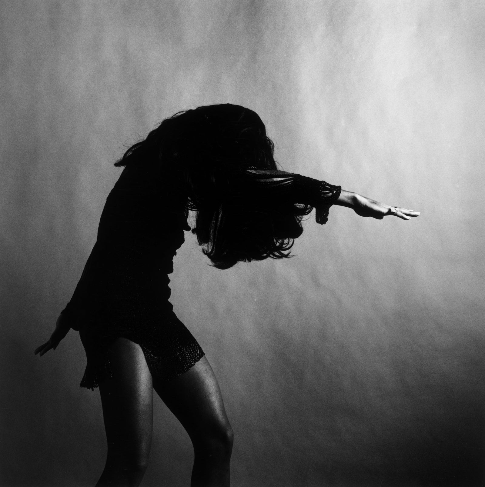Black and white studio photograph of Tina Turner bending forward mid-dance, one arm outstretched and hair over her face, 1969
