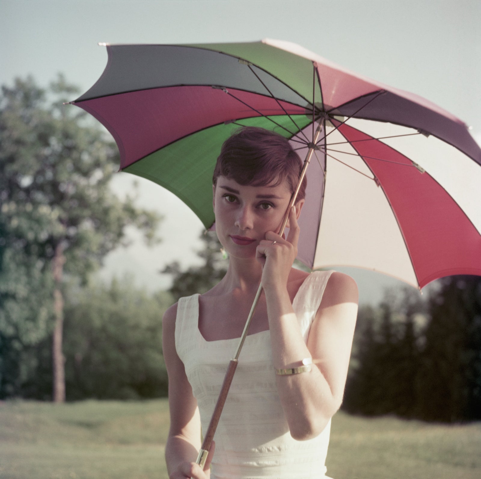 Colour photograph of Audrey Hepburn in a white top holding a multicoloured umbrella on a golf course in Switzerland, 1954