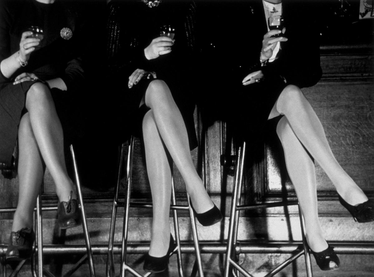 Black and white photograph of three pairs of crossed stockinged legs in high heels on bar stools, 1946