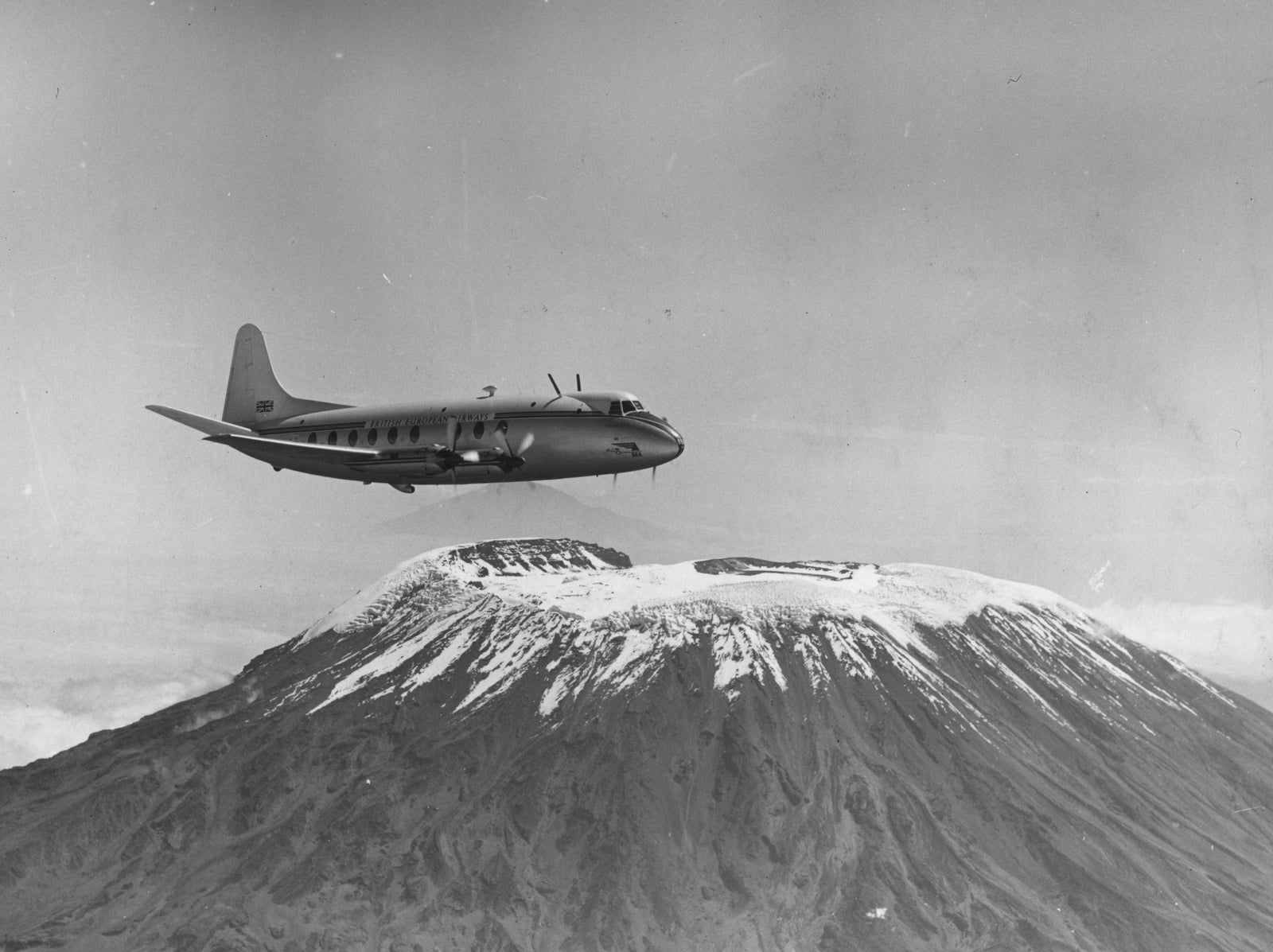 Black and white photograph of a Vickers Viscount aeroplane flying above the snow-capped summit of Mount Kilimanjaro, 1950
