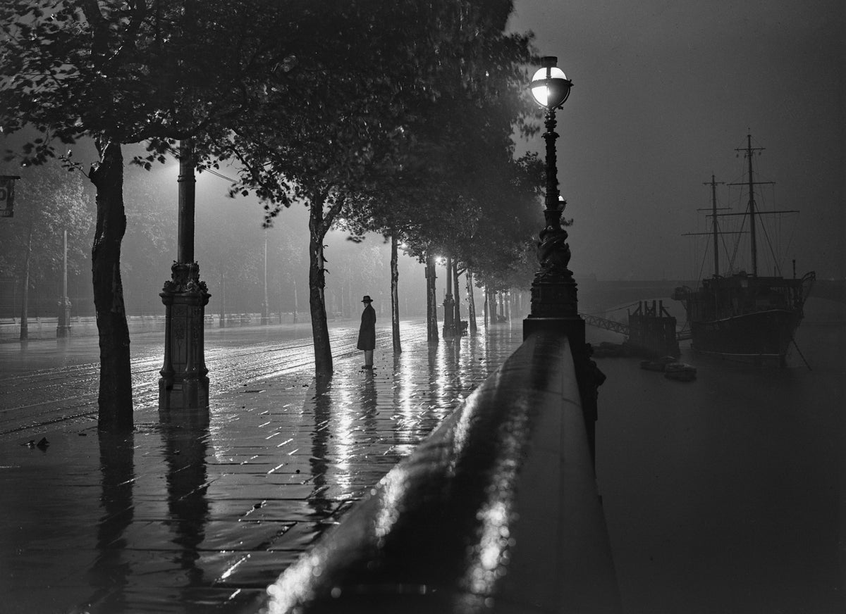 Black and white photograph of a lone figure on the rain-soaked Thames Embankment at night under street lamps, London, 1929