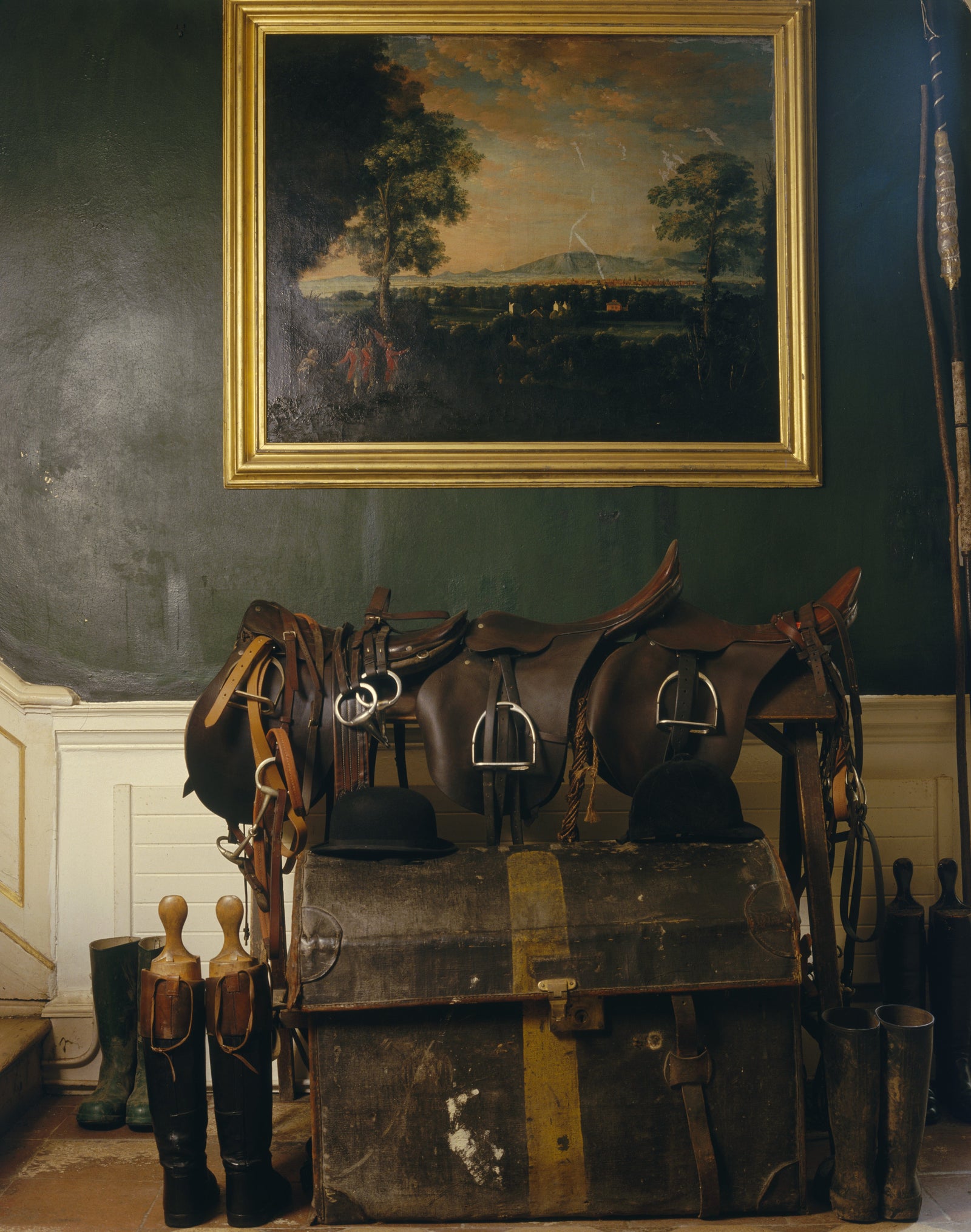 Colour photograph of antique saddles and an old trunk beneath a gilt-framed oil painting inside Leixlip Castle, County Kildare