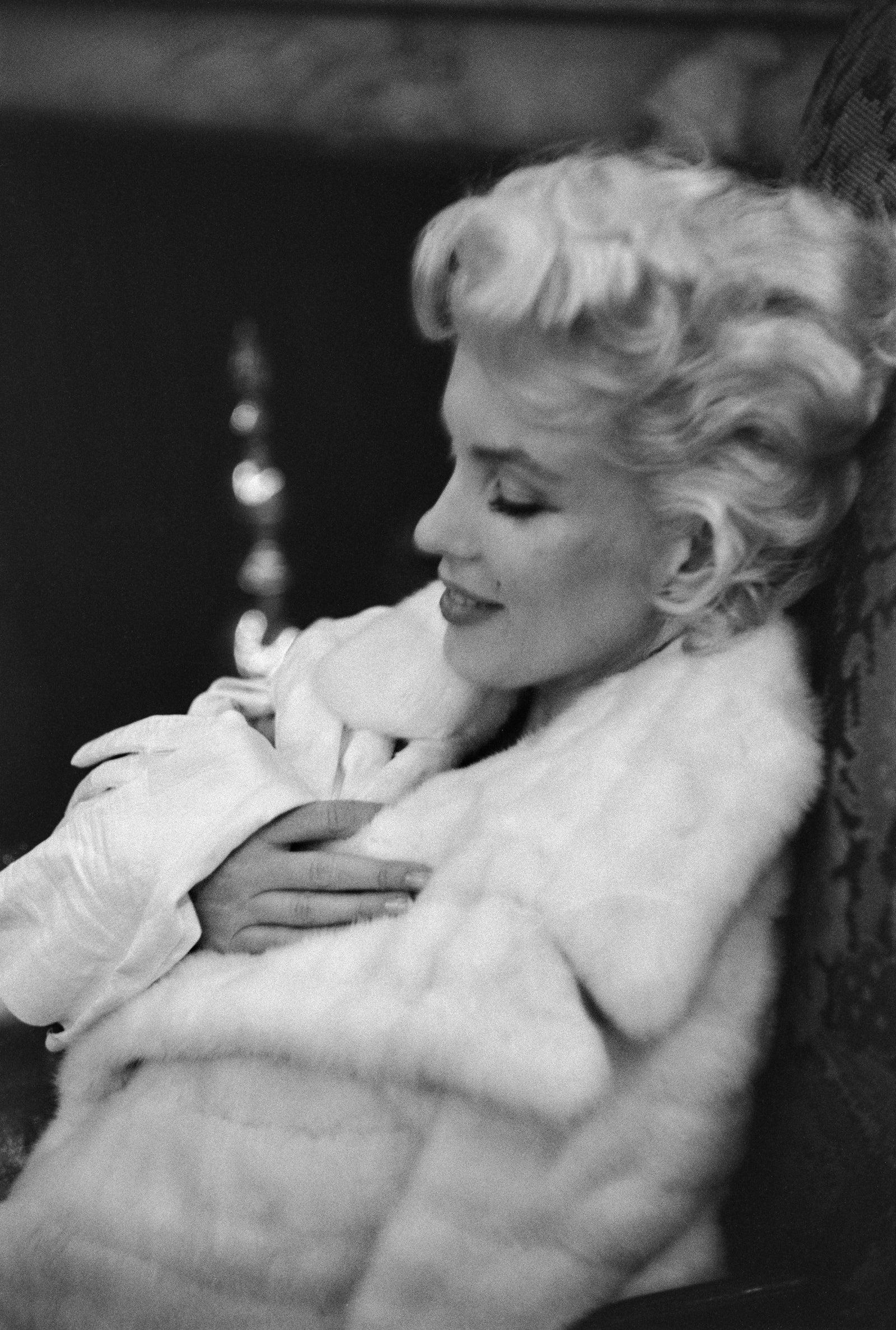 Black and white photograph of Marilyn Monroe with eyes closed wrapped in a white fur coat, New York, 1955
