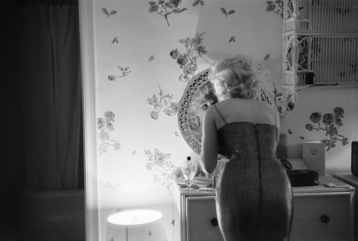 Black and white photograph of Marilyn Monroe seen from behind in a fitted dress at her dressing table at the Ambassador Hotel, New York, 1955