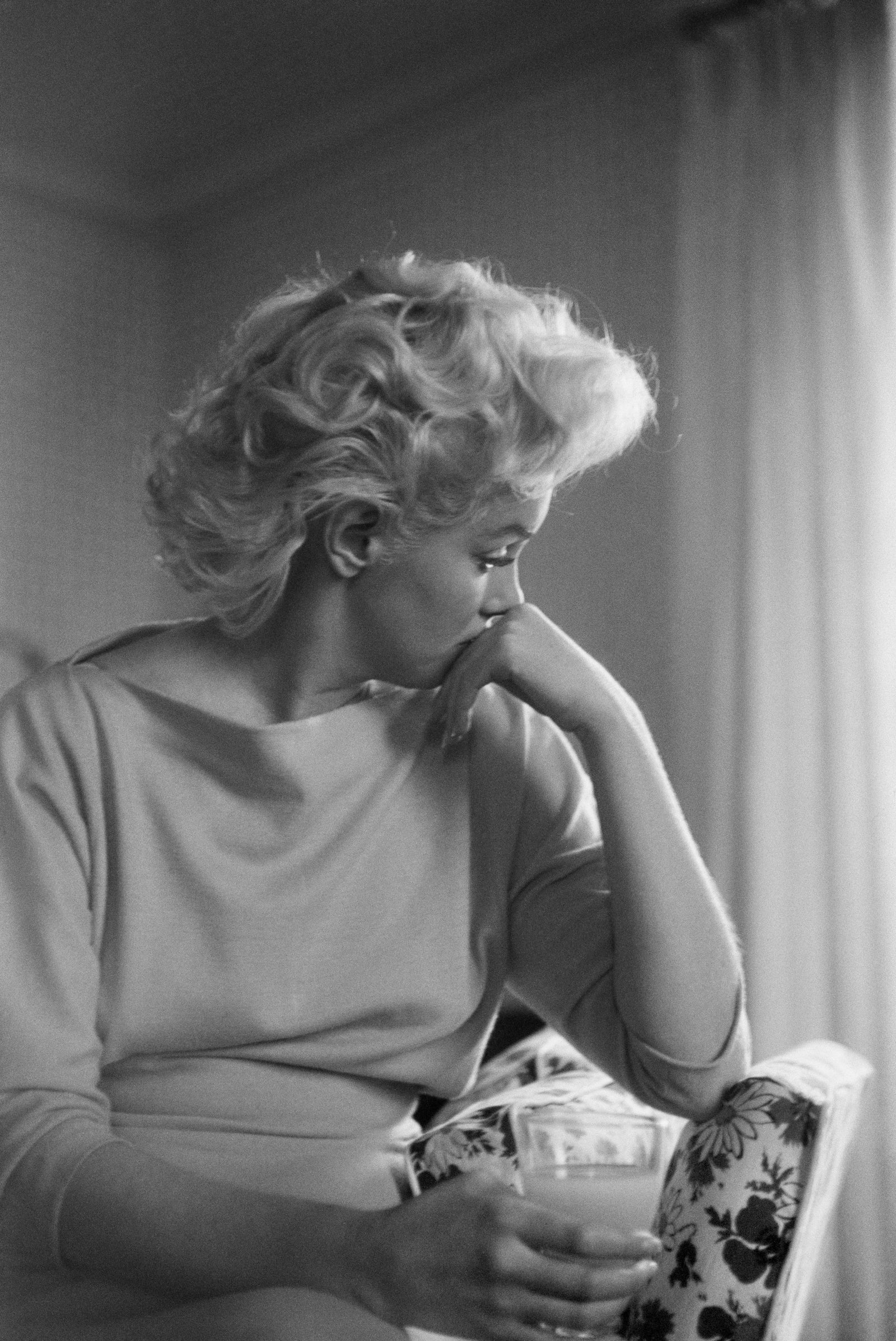 Black and white photograph of a pensive Marilyn Monroe resting her chin on her hand at the Ambassador Hotel, New York, 1955