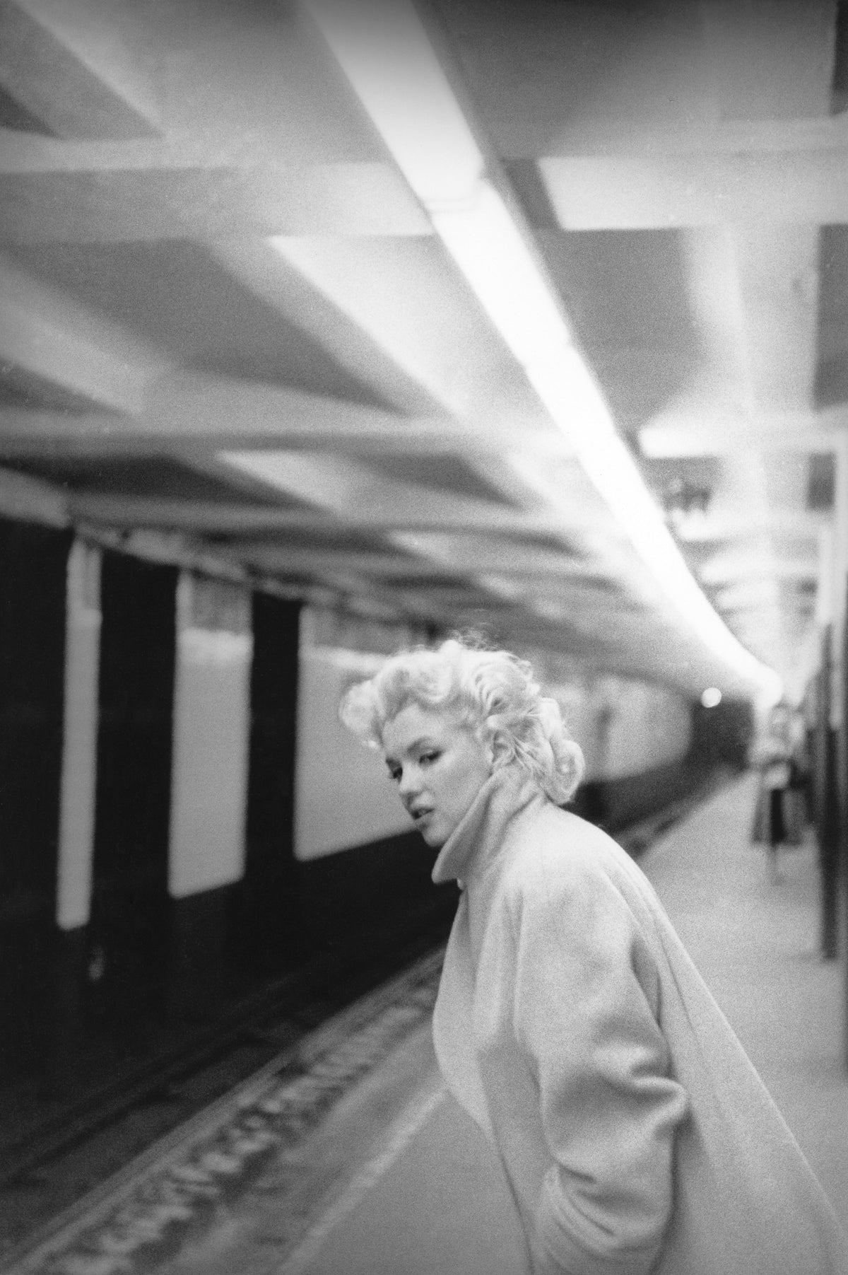 Black and white photograph of Marilyn Monroe in a pale coat on an empty subway platform at Grand Central, New York, 1955